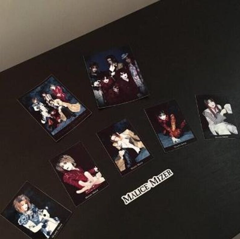 May include: A collection of eight black and white photos of a Japanese rock band called Malice Mizer. The photos are arranged on a black surface. The band members are wearing dark clothing and makeup.