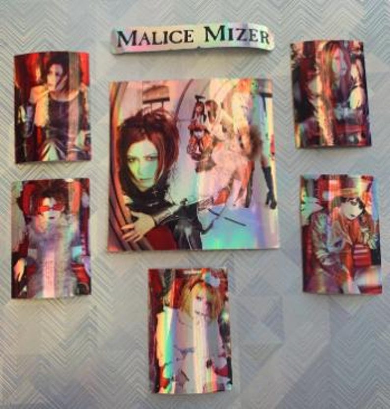 Op de afbeelding: Een set van zeven holografische stickers met de band Malice Mizer. De stickers zijn rechthoekig en bevatten verschillende afbeeldingen van de bandleden. De stickers zijn gerangschikt in een rasterpatroon op een witte achtergrond.