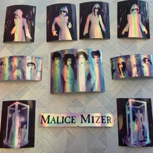 Op de afbeelding: Een verzameling van negen holografische stickers met de band Malice Mizer. De stickers zijn rechthoekig en tonen afbeeldingen van de bandleden in verschillende poses. De stickers zijn iriserend en hebben een regenboog-effect.