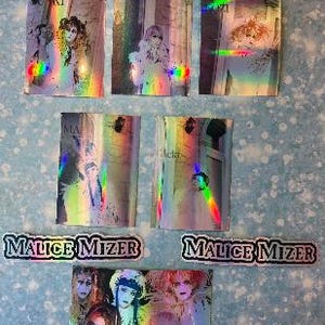 May include: A set of 7 holographic trading cards featuring the Japanese rock band Malice Mizer. The cards feature different band members in various poses. The cards are in a rainbow holographic finish.