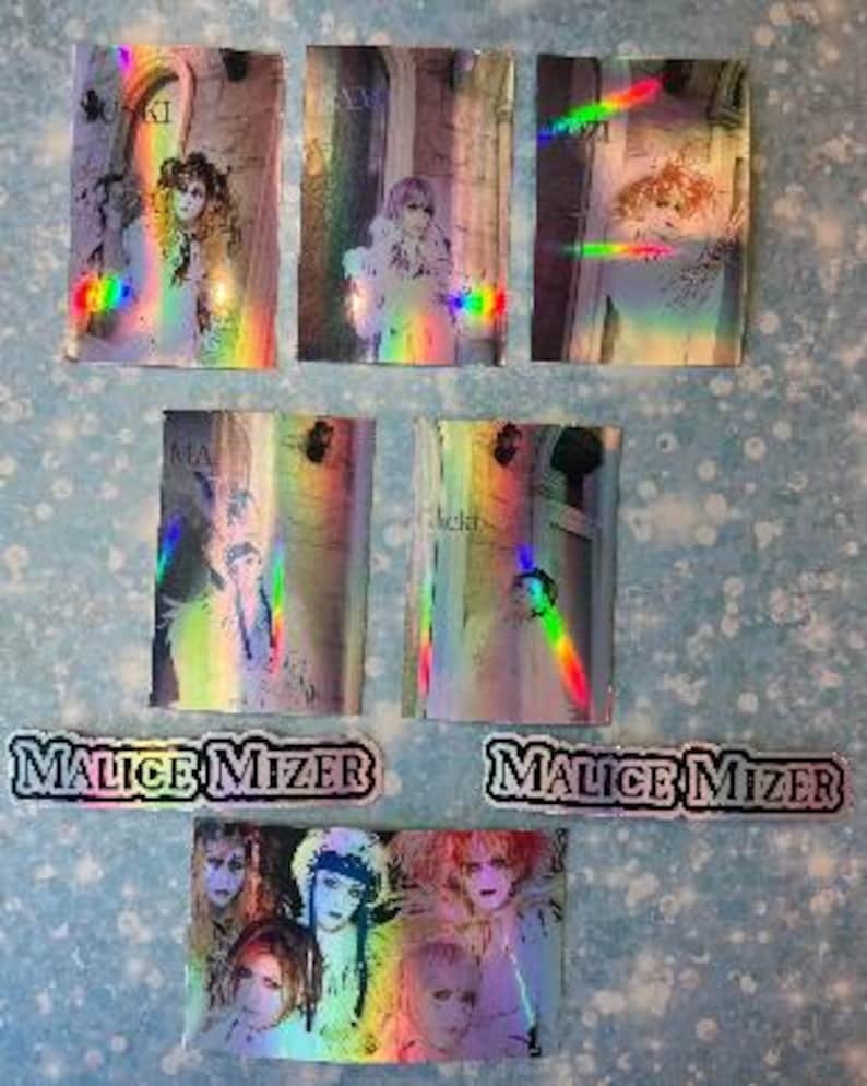 May include: A set of 7 holographic trading cards featuring the Japanese rock band Malice Mizer. The cards feature different band members in various poses. The cards are in a rainbow holographic finish.