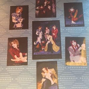 May include: A set of seven black and white photos of a Japanese rock band. The photos feature the band members in various poses and outfits. The band's name is written in Japanese on the bottom of each photo.
