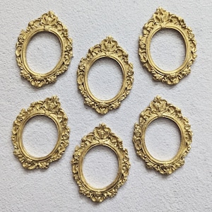 May include: A set of five small, oval-shaped picture frames in a metallic gold finish. Each frame features an ornate, raised relief pattern along the border with decorative scrollwork and floral-inspired detailing at the top and bottom edges.