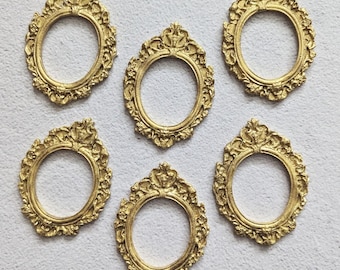 May include: A set of five small, oval-shaped picture frames in a metallic gold finish. Each frame features an ornate, raised relief pattern along the border with decorative scrollwork and floral-inspired detailing at the top and bottom edges.
