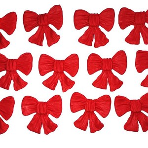 May include: A collection of thirteen bright red bows, each with a classic bow shape. The bows are arranged against a white background. The bows are made of a textured material.