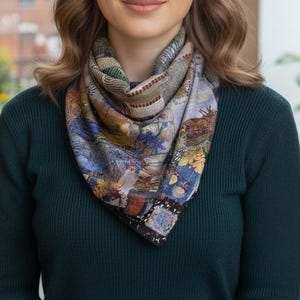 Peut inclure: Un foulard en soie coloré avec un motif floral et abstrait. Le foulard présente un mélange de bleus, de verts, de jaunes et de bruns. Il est porté autour du cou avec un pull vert foncé.