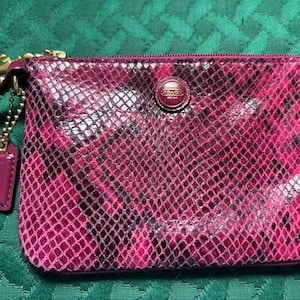 May include: A pink snakeskin clutch purse with a gold chain and a gold Coach logo.