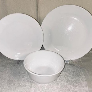 May include: A white dinnerware set featuring a large plate, a medium plate, and a bowl. The plates and bowl are all white and have a simple, clean design. The set is likely for serving meals.