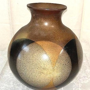 May include: A brown ceramic vase with a rounded body and a narrow neck. The vase features a geometric design with sections of black, tan, and beige. The vase has a glossy finish and is suitable for home decor.