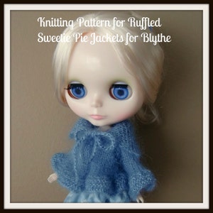 May include: A blue knitted jacket with a ruffled trim, designed for a Blythe doll. The jacket has a bow at the neckline and is worn by a doll with blonde hair and blue eyes.