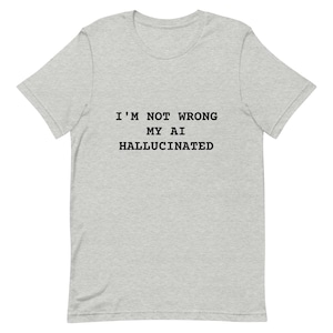 May include: A pale grey t-shirt featuring the black text "I'M NOT WRONG MY AI HALLUCINATED". The shirt has a round neck and short sleeves. The material looks soft and comfortable.