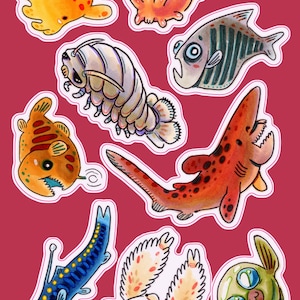 May include: A set of ten colorful stickers featuring various sea creatures, including a shark, a fish, a crab, and a sea slug. The stickers are all hand-painted and have a whimsical, cartoonish style.
