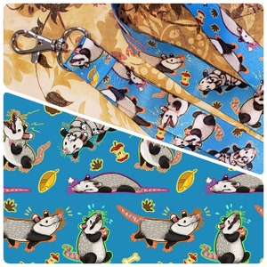May include: A blue and white lanyard with a repeating pattern of opossums and apples. The opossums are in various poses, including running, jumping, and standing. The lanyard is made of a durable material and is perfect for holding keys, badges, or other small items.