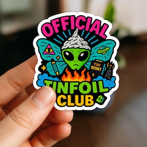 May include: A colorful sticker featuring a green alien wearing a tinfoil hat, with the words "OFFICIAL TINFOIL CLUB." The design includes a triangle with an eye, a UFO, flames, and the words "TOP SECRET."