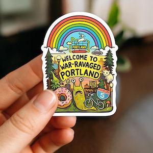 Może przedstawiać: Kolorowa naklejka z tęczą nad sceną z Portland. Zawiera pączka, ślimaka, rower i napis "Welcome to War-Ravaged Portland".