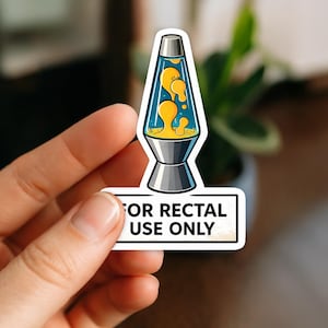 Peut inclure: Un autocollant représentant une lampe à lave de dessin animé avec un verre bleu, de la lave jaune et une base argentée. Le texte "FOR RECTAL USE ONLY" est inscrit en noir sur un fond blanc.