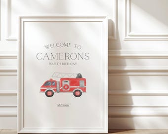May include: Framed print featuring a red fire engine illustration. The print includes the text "WELCOME TO CAMERONS FOURTH BIRTHDAY" and the date 05.15.2026. The frame is white, and the background is a light colour.