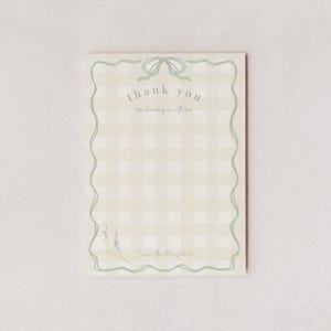Puede incluir: Tarjeta de agradecimiento rectangular con un fondo de patrón de cuadros vichy verde claro. La tarjeta tiene un borde verde claro con un lazo en la parte superior y un diseño floral en la parte inferior. Las palabras "thank you" están escritas en una fuente de guion.