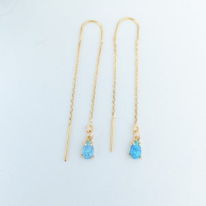 May include: A pair of gold chain earrings with blue opal teardrop charms. The earrings are delicate and feminine.