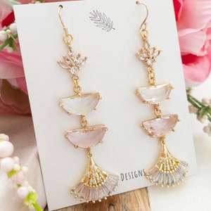 May include: A pair of gold tone dangle earrings with pink and clear crystal stones. The earrings feature a fan-shaped design at the bottom and have a delicate, feminine look.
