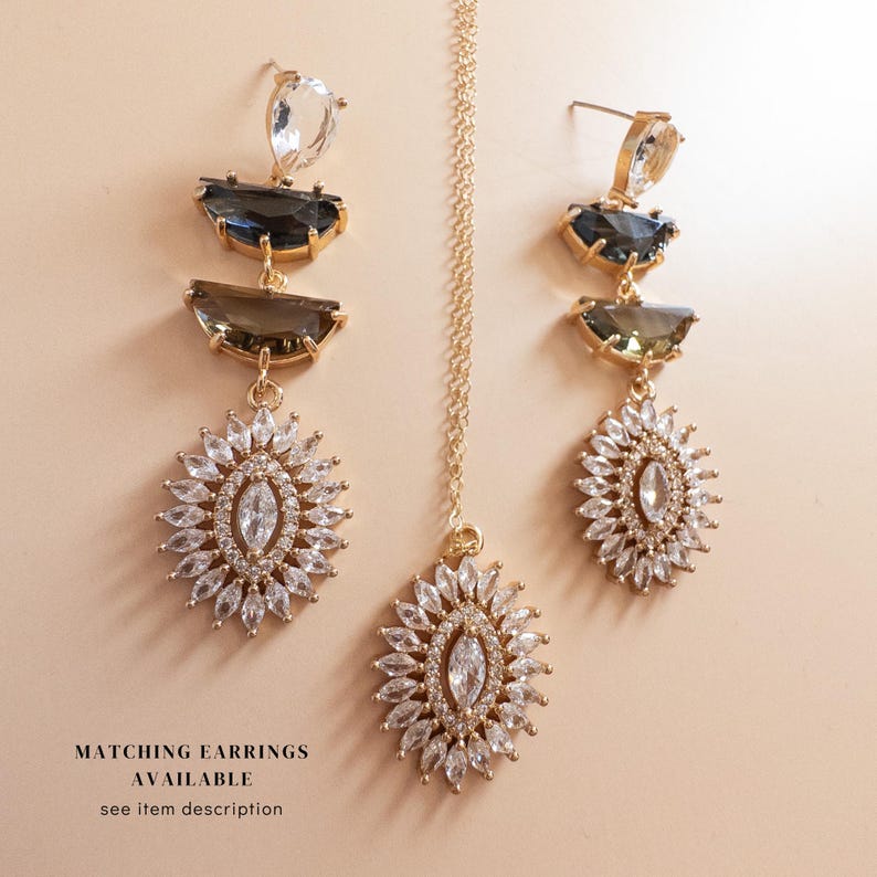 May include: A gold-toned jewelry set featuring a necklace and earrings. The earrings and pendant have a sunburst design with clear and dark-colored gemstones. The image includes the text "MATCHING EARRINGS AVAILABLE see item description."