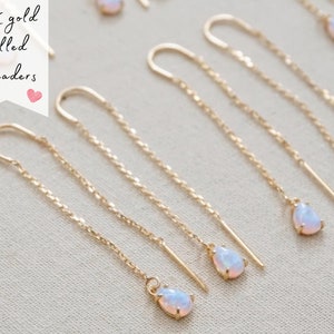 May include: Six pairs of 14K gold filled threader earrings with teardrop-shaped opal stones. The earrings are delicate and feminine.