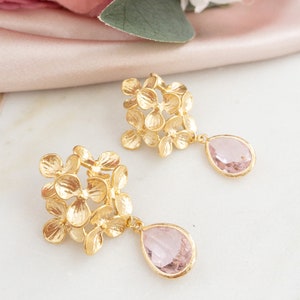 Peut inclure: Boucles d'oreilles en forme de fleur dorées avec des cristaux en forme de larme roses.