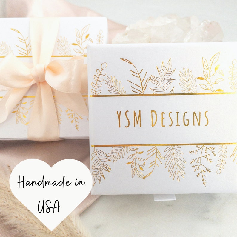 May include: Two white gift boxes with gold leaf designs and the text "YSM DESIGNS". One box is tied with a peach ribbon. The image also includes a heart-shaped graphic that says "Handmade in USA".