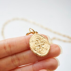 May include: Gold chain necklace with a large oval pendant featuring a detailed, embossed cross design.