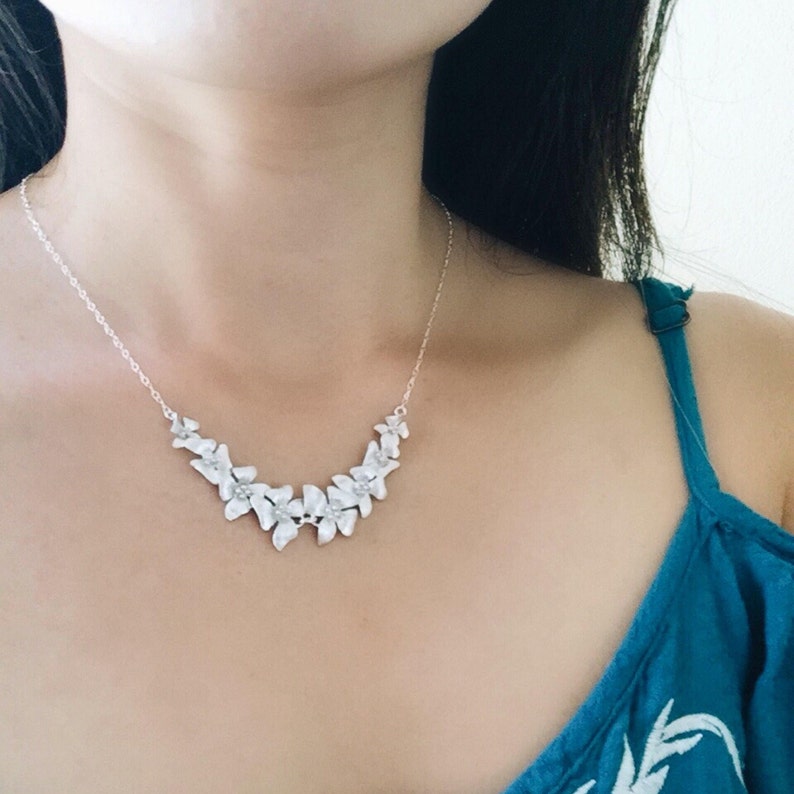 May include: A silver necklace with a delicate chain and a floral design. The flowers are arranged in a curved shape and have a white finish.