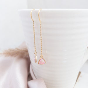 Dainty chain earrings with triangular pink opal stones dangling from a white mug.