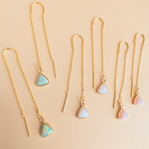 May include: Gold-colored threader earrings with triangular opal pendants. The earrings have a delicate chain design and a small bar at the end. The opal pendants are in shades of blue, white, and pink.