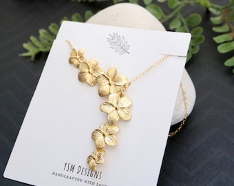 May include: Gold necklace with a cascading design of five flower charms. The necklace is displayed on a white card with the text "YSM DESIGNS HANDCRAFTED WITH LOVE".