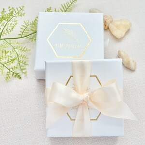 May include: Two white gift boxes with gold lettering. The top box has the text "YSM Designs" and the bottom box has a gold ribbon tied in a bow.