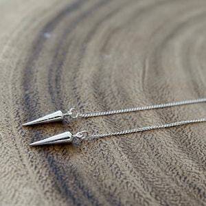 May include: A pair of silver dangle earrings with a pointed cone shape at the end of each chain.