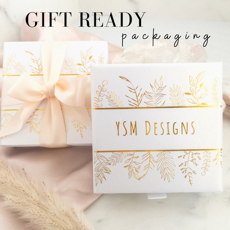 May include: White gift box with a gold ribbon and a gold floral design. The box is labelled "YSM DESIGNS" and says "GIFT READY packaging" at the top.