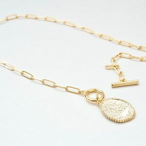 May include: A gold chain necklace with a textured oval pendant. The chain is made of small, linked ovals.
