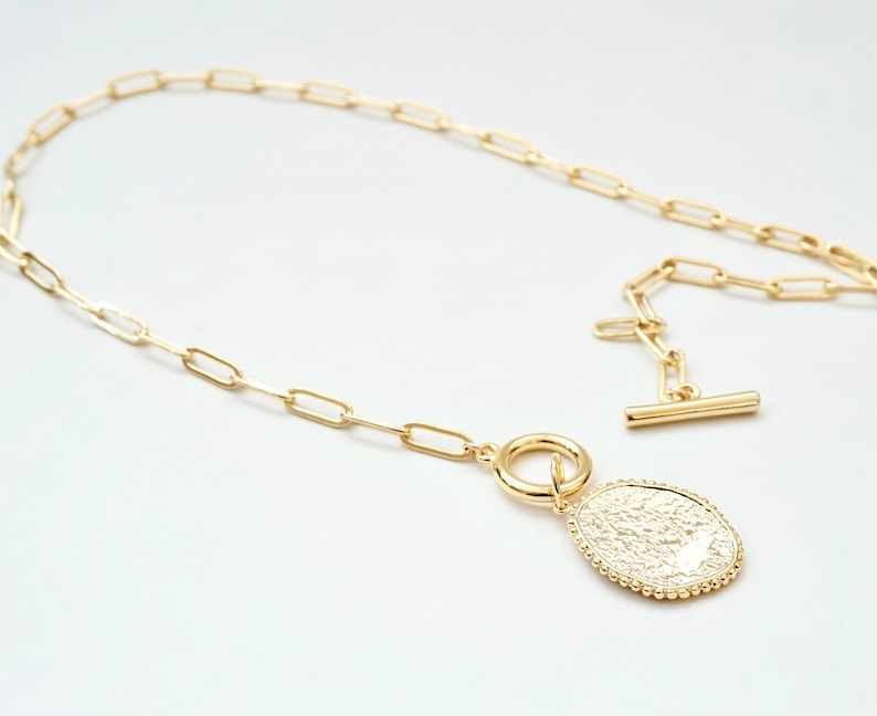 May include: A gold chain necklace with a textured oval pendant. The chain is made of small, linked ovals.