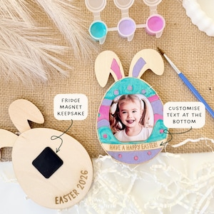 May include: Wooden Easter egg-shaped fridge magnet keepsake with bunny ears. The egg has a photo frame with a child's picture and the text "Have a Happy Easter!". Includes paint and a paintbrush. The text "Easter 2026" is on the magnet.