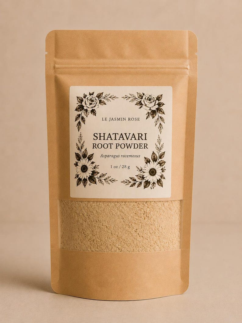 May include: A brown paper bag with a clear window displaying a tan powder. The bag has a white label with the text "LE JASMIN ROSE" and "SHATAVARI ROOT POWDER" in a floral design. The label also states "1 oz / 28 g".