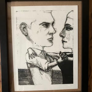 Może przedstawiać: Oprawiona czarno-biała grafika przedstawiająca dwie postacie w bliskim uścisku. Grafika, w czarnej ramie, przedstawia mężczyznę i kobietę w stylizowanej, artystycznej formie. Grafika umieszczona jest na neutralnym tle, co podkreśla kontrast postaci.