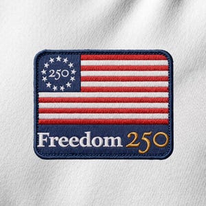 May include: Embroidered patch featuring a stylized American flag design. The patch has a blue border, red and white stripes, and a blue field with stars and the number "250". The text "Freedom 250" is displayed in gold.