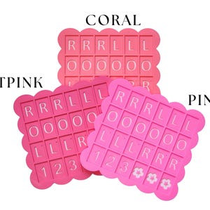 May include: Three pink silicone molds with scalloped edges, each featuring letter and number cutouts. The molds are labeled "CORAL", "HOTPINK", and "PINK". The letters and numbers are in white.