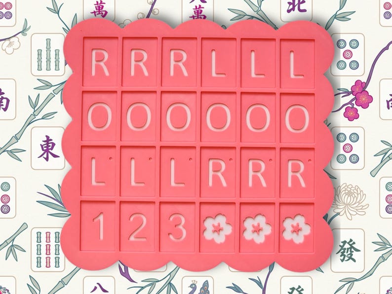 May include: A coral-colored, scalloped-edge mold for making decorative tiles. The mold has a grid of rectangular spaces with the letters R, L, and O, numbers 1, 2, and 3, and flower designs. The background features a floral and Mahjong tile pattern.