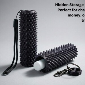 May include: Black cylindrical storage container with a textured, spiky exterior. One container is open, revealing a white object inside. Includes a black lanyard and a keyring. Text on the image reads: "Hidden Storage Inside! Perfect for chapstick, money, or small trinkets."