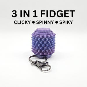 May include: A purple gradient 3 in 1 fidget keychain with the text 3 IN 1 FIDGET CLICKY SPINNY SPIKY. The cylindrical object features a textured spiky surface, a flat top button, and a dark metal lobster clasp attached to a split ring.
