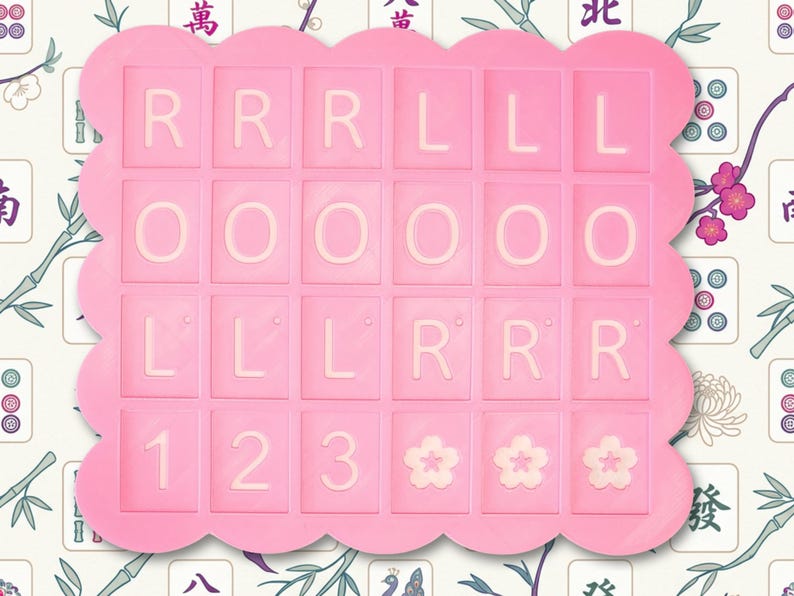 May include: A pink, scalloped-edged tray with a grid of lettered and numbered tiles. The tiles spell out "RRR LLL OOO LLL RRR 123" and feature three flower designs. The background has a floral and Asian-inspired pattern.