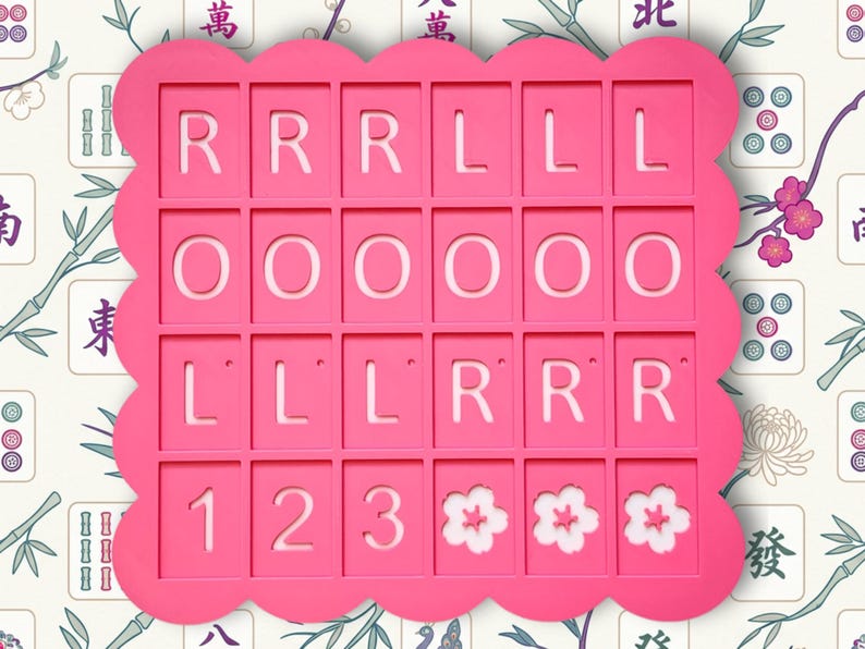 May include: A bright pink, scalloped-edge game board with cut-out squares. The squares contain the letters R, O, and L, along with the numbers 1, 2, and 3, and three white flower designs. The background features a floral and bamboo pattern.