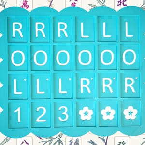 May include: A turquoise-colored game piece holder with a scalloped edge, holding white letter and number tiles. The tiles spell out "RRR LLL OOO LLL RRR 123" and feature three flower symbols. The background has a floral pattern.