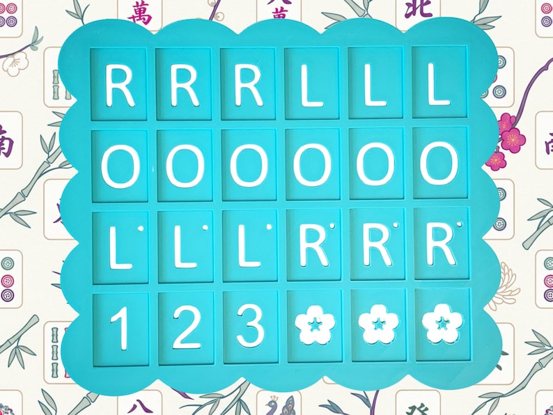 May include: A turquoise-colored game piece holder with a scalloped edge, holding white letter and number tiles. The tiles spell out "RRR LLL OOO LLL RRR 123" and feature three flower symbols. The background has a floral pattern.